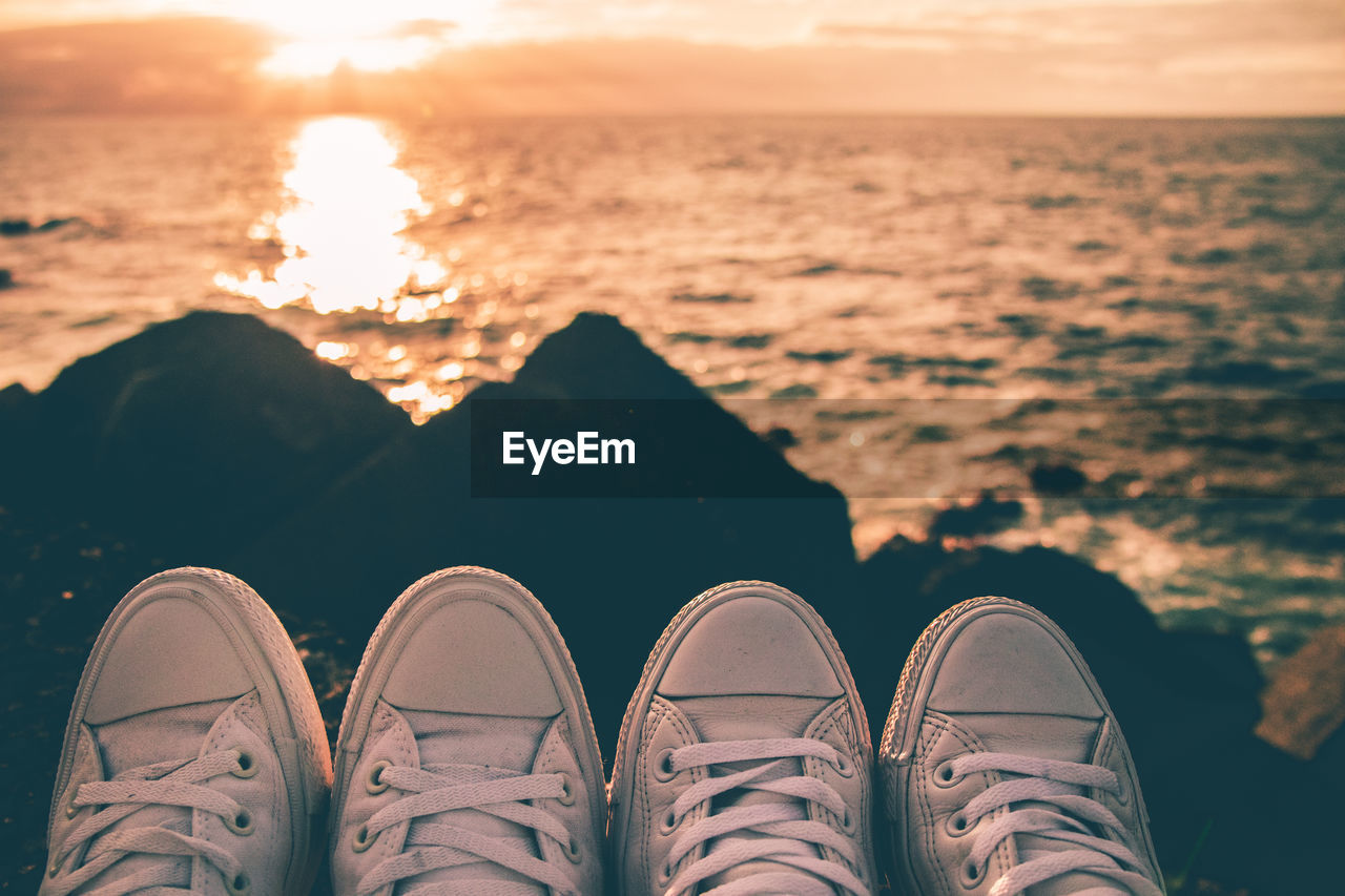 Low section of couple wearing shoes by sea