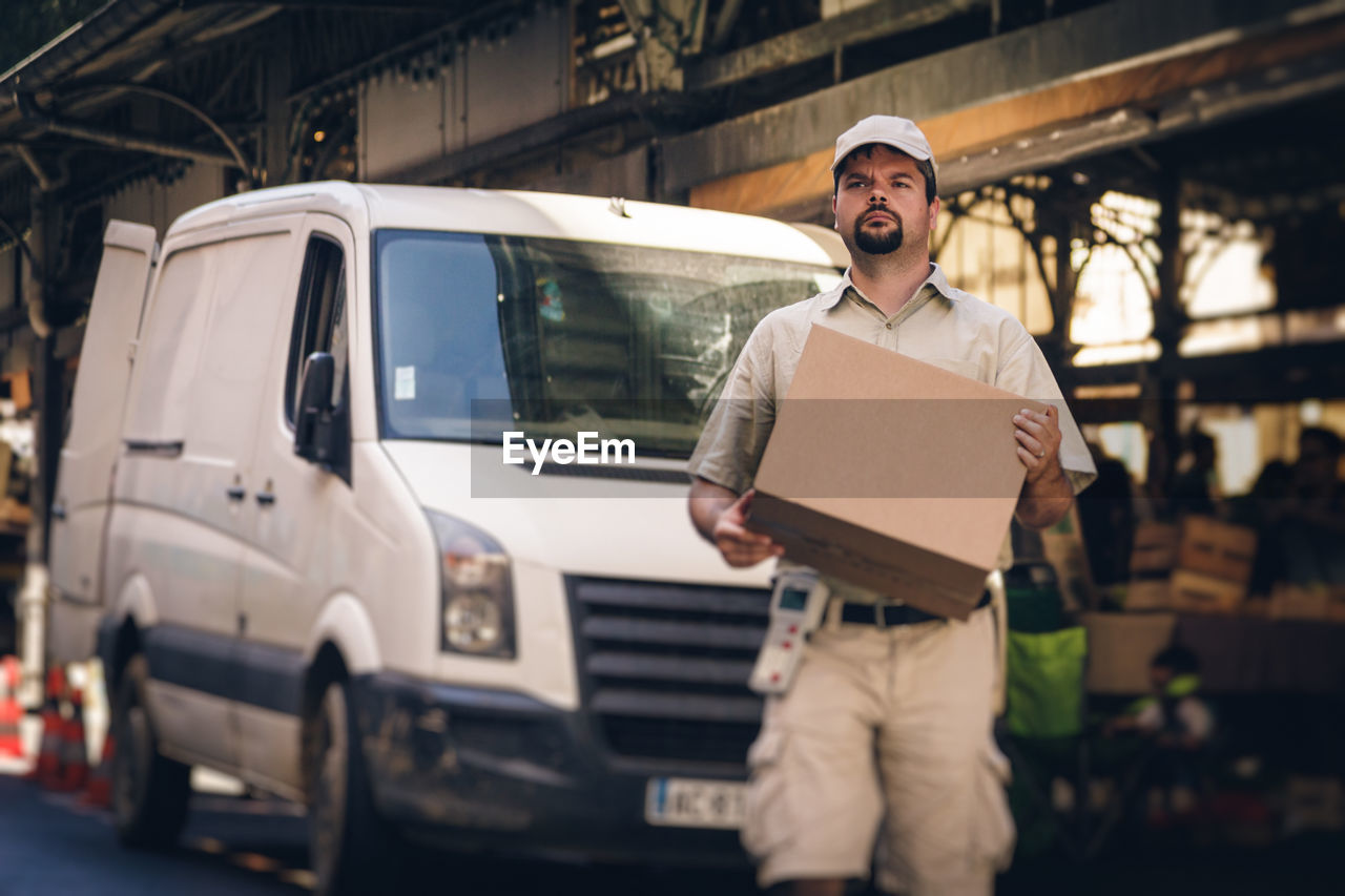Delivery man holding cardboard box while walking on street