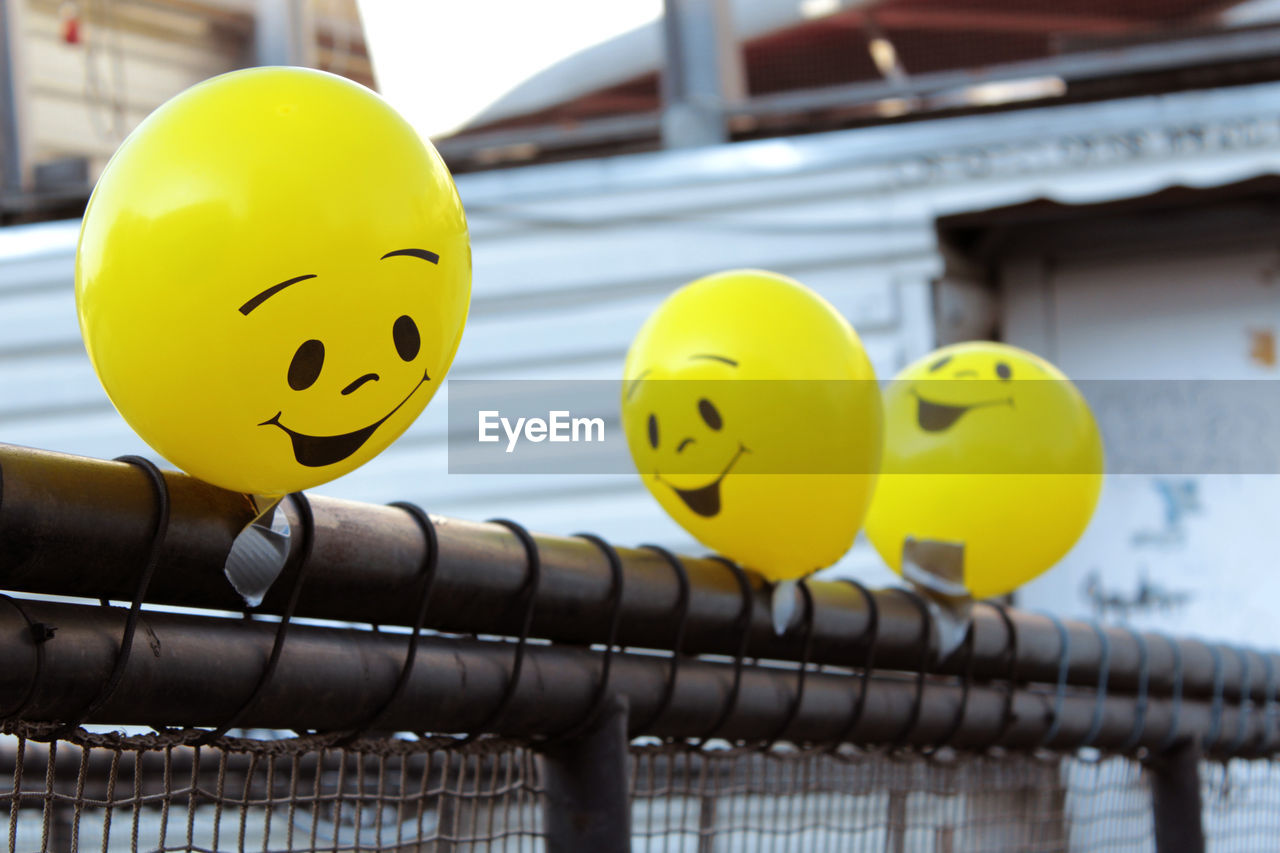 Three yellow balloons with smiley faces on a fence