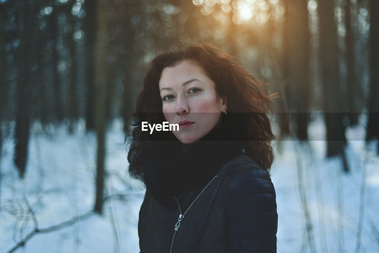 Portrait of young woman standing in forest during winter