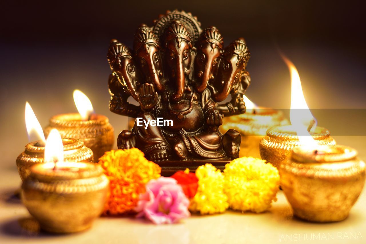 Close-up of ganesha idol with flowers and candles on table