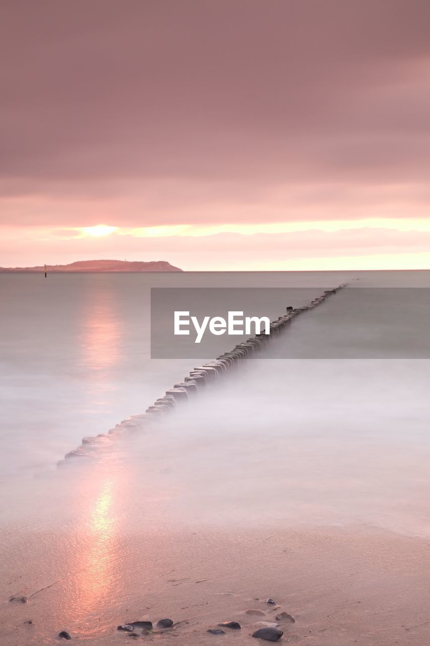 Wooden breakwater in wavy baltic sea. romantic atmosphere at smooth wavy sea. pink horizon 