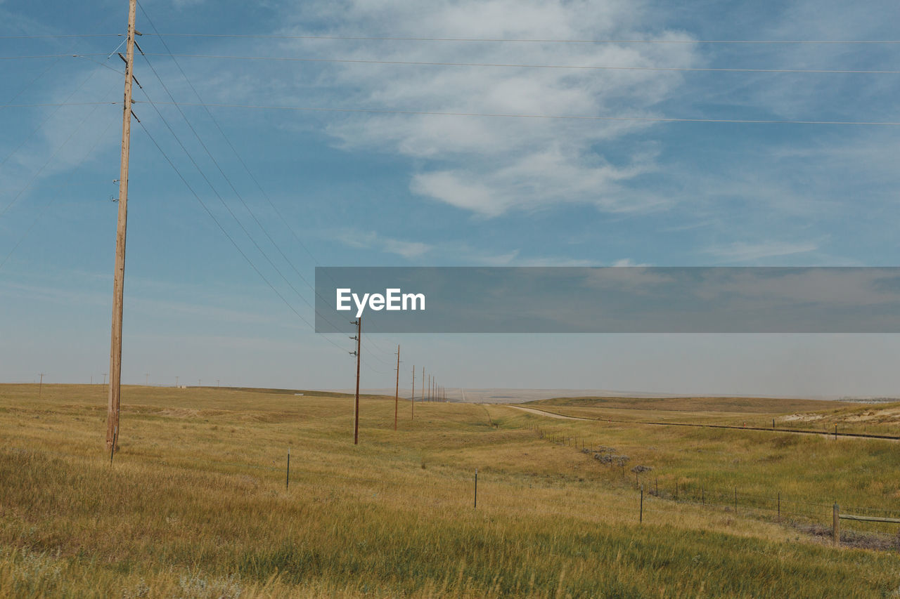 Scenic view of field against sky, power lines