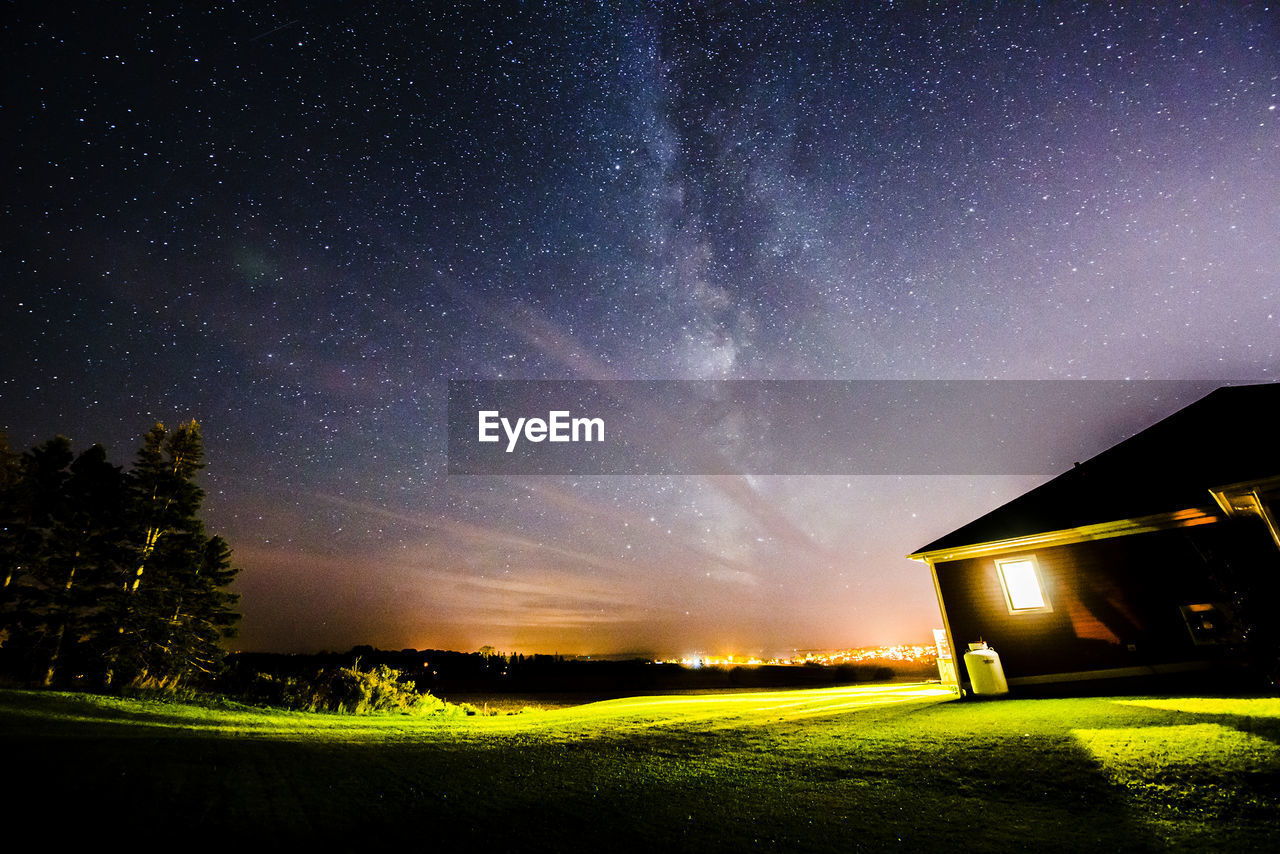 Low angle view of illuminated house on grassy field against starry sky