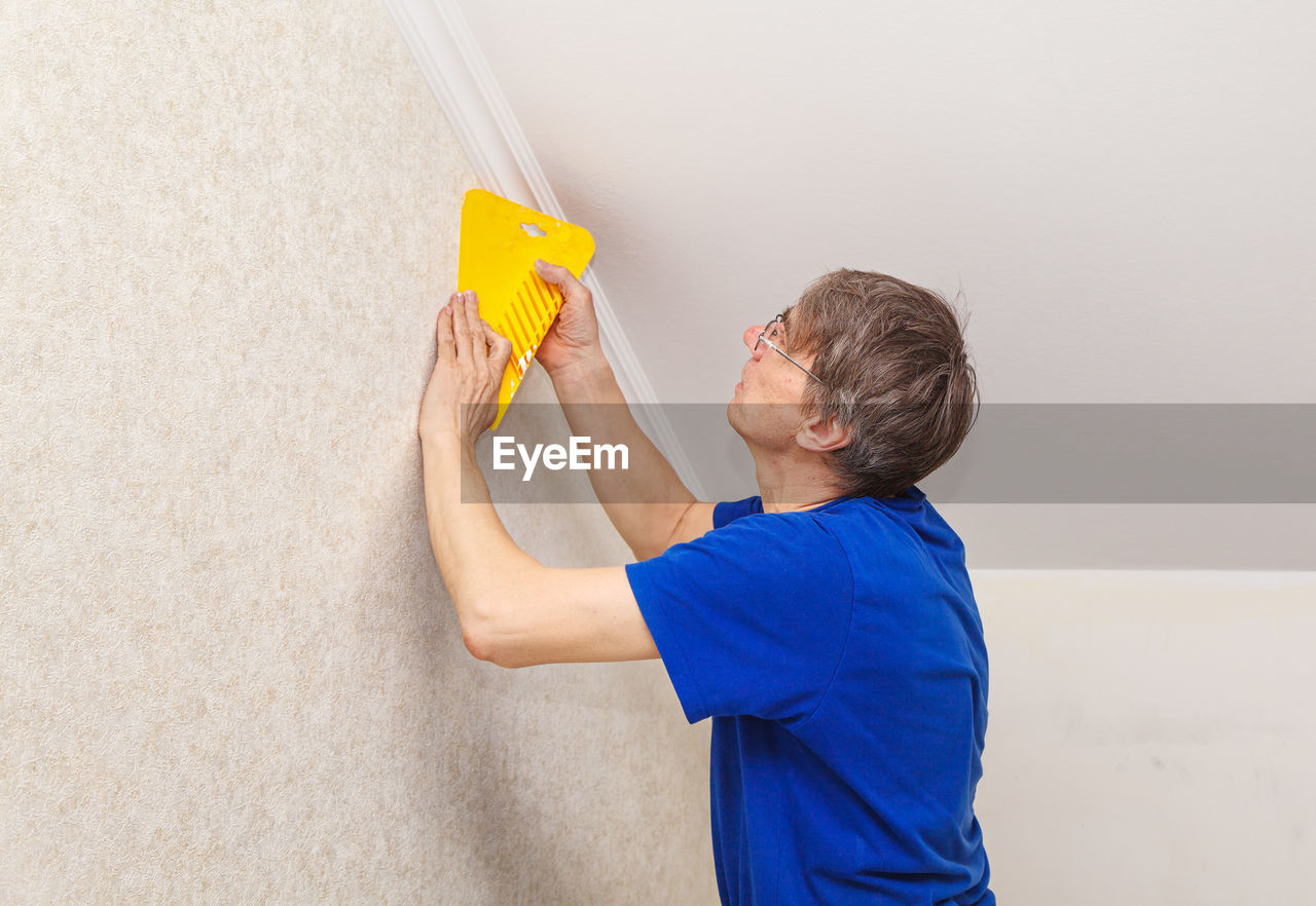 Mature painter using scrapper on wall