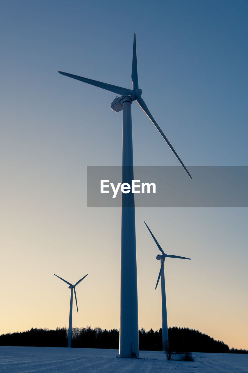 Low angle view of windmills against clear sky in winter