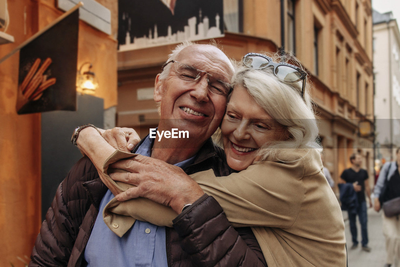 Happy senior woman hugging man from behind in city