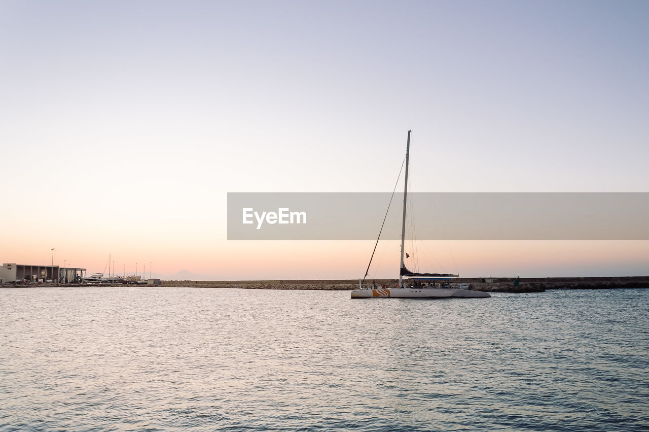 BOATS SAILING IN SEA AT SUNSET