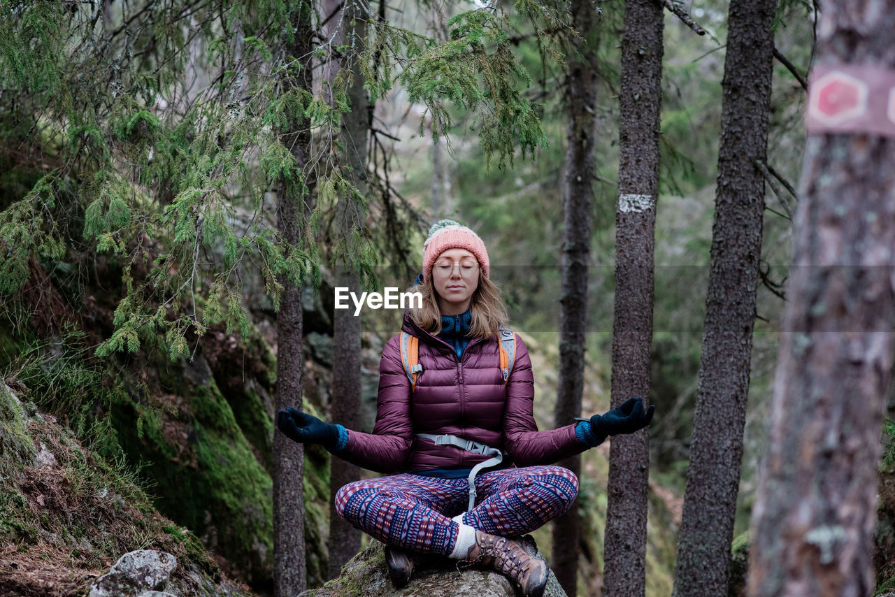 Woman solo hiking whilst meditating on a rock in a forest