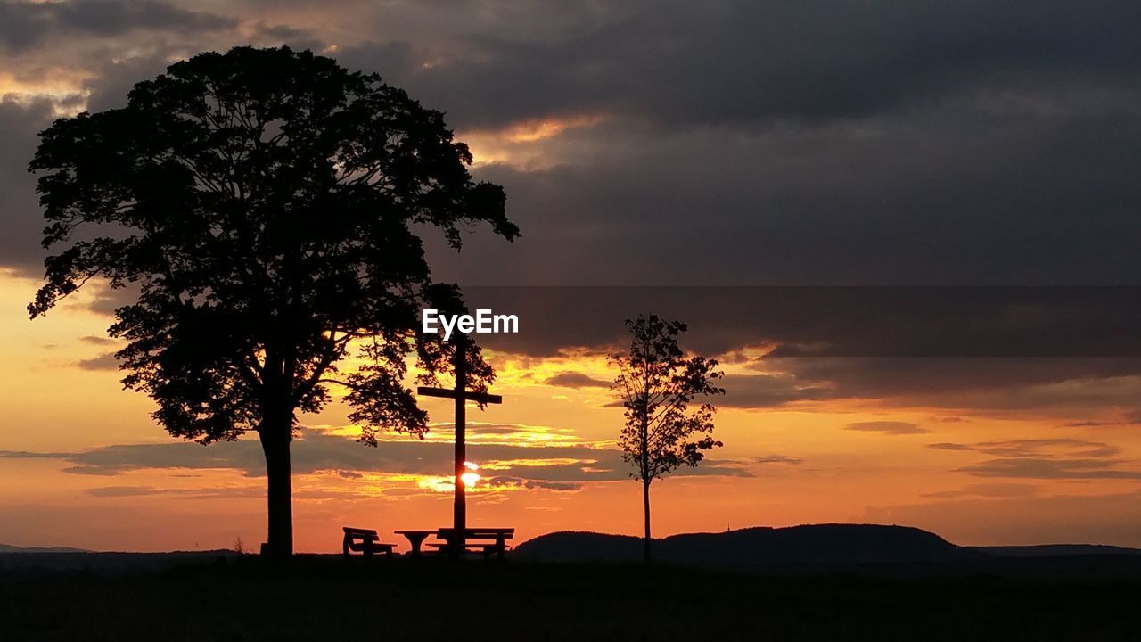 Silhouette trees on field against dramatic sky