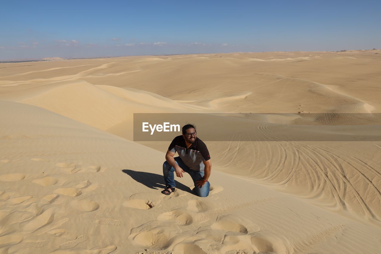 Full length of man kneeling on sand dune in desert