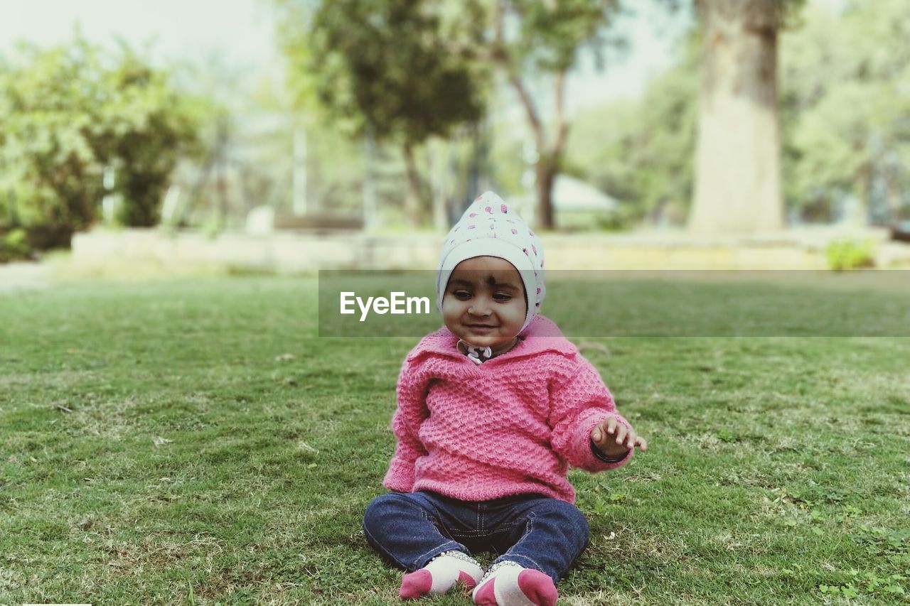 Full length of cute baby girl wearing warm clothing sitting on field at park