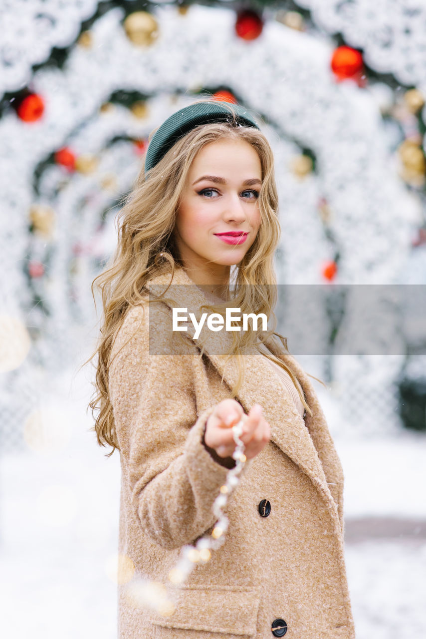 A cute young woman holds in her hand the lights of a garland on the background of a christmas market