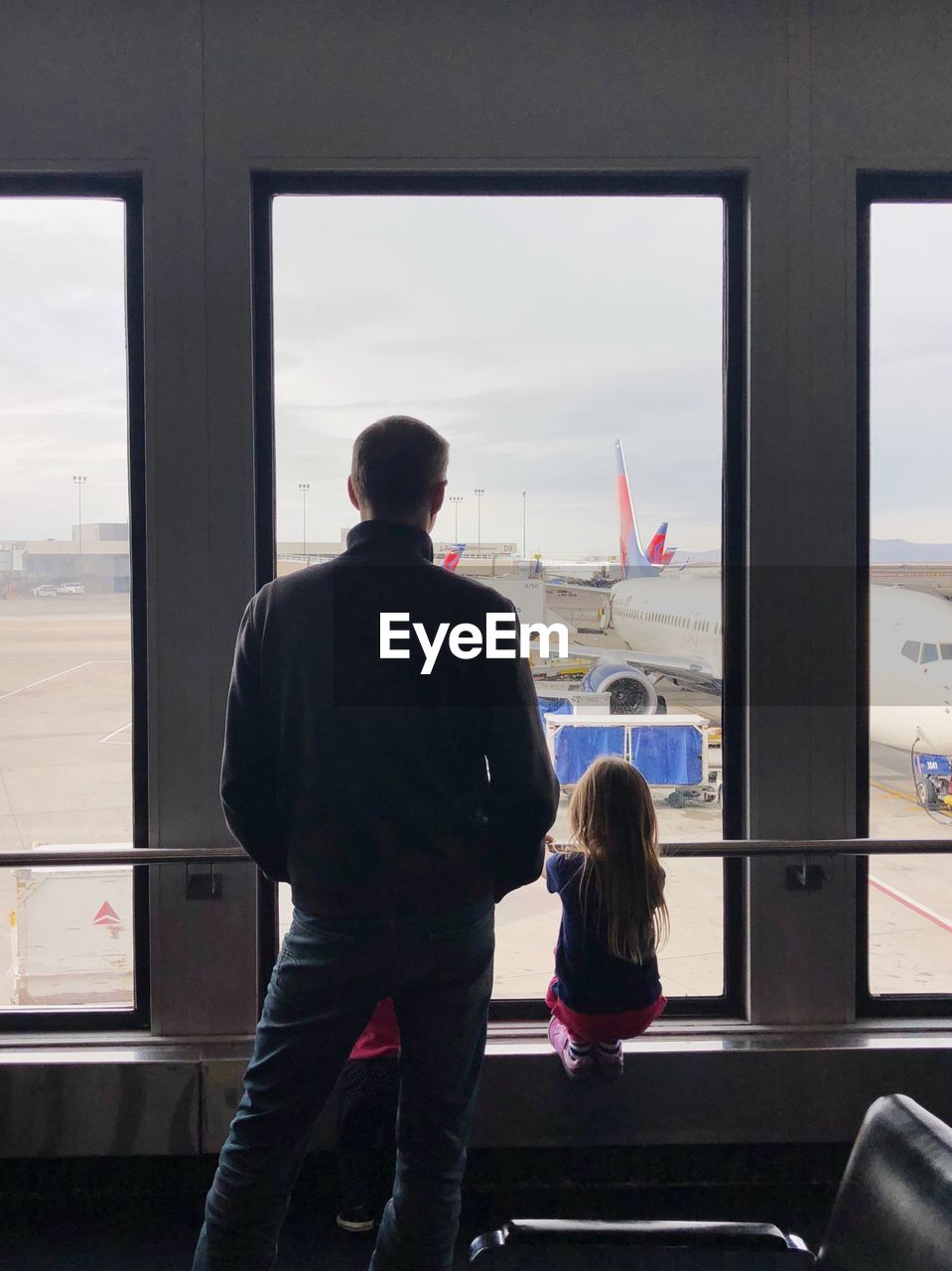 REAR VIEW OF PEOPLE LOOKING AT AIRPLANE WINDOW