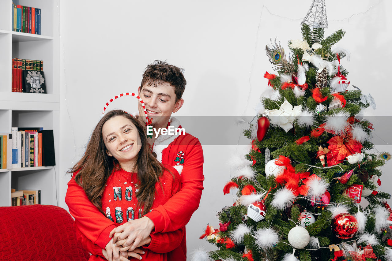 Smiling couple standing by christmas tree at home