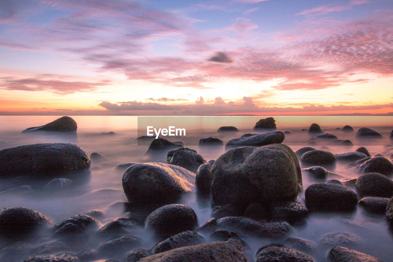 Rocks on beach against sky during sunset