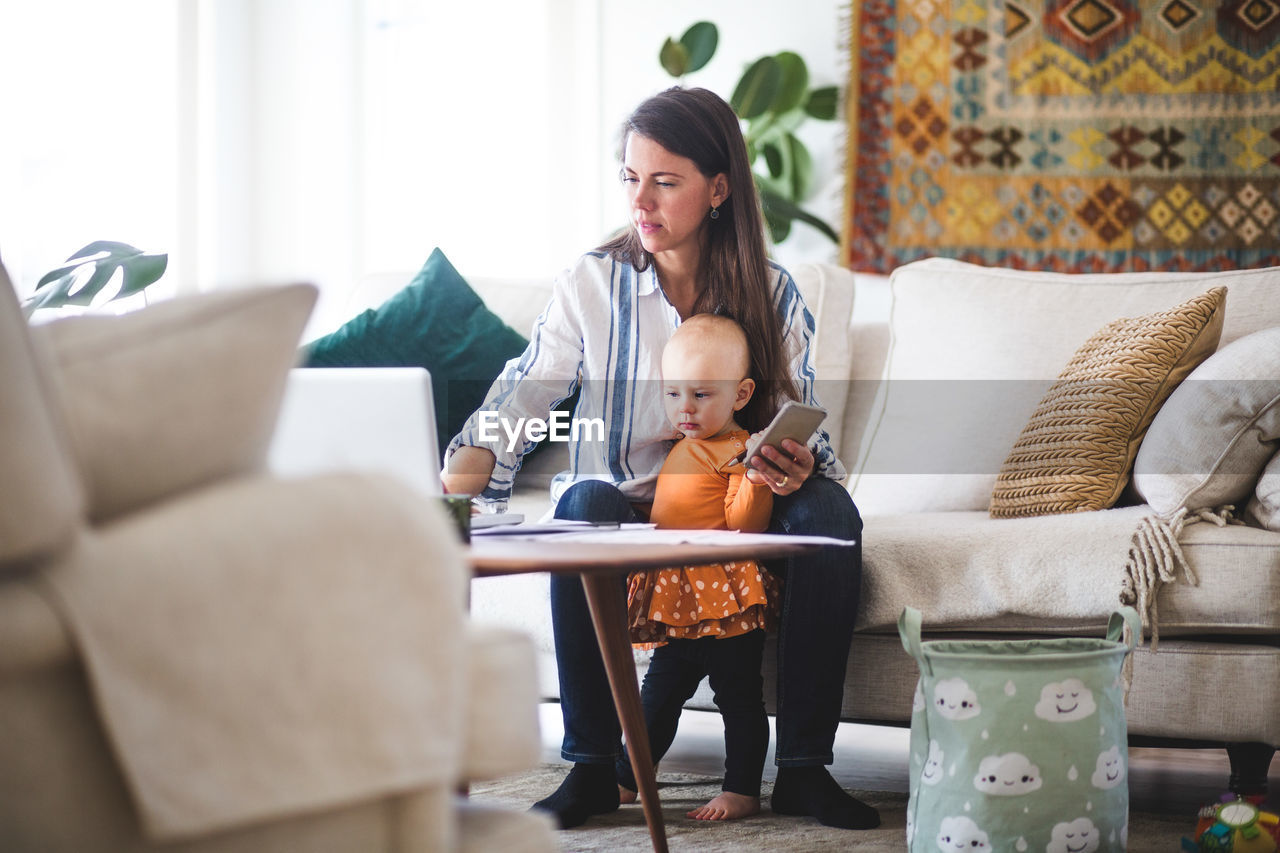 Multi-tasking mother using laptop while taking care of daughter in living room