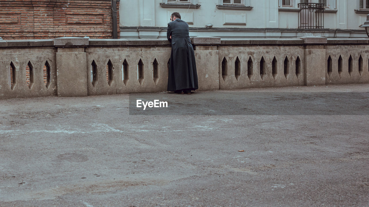 SIDE VIEW OF MAN STANDING AGAINST BUILDINGS IN CITY