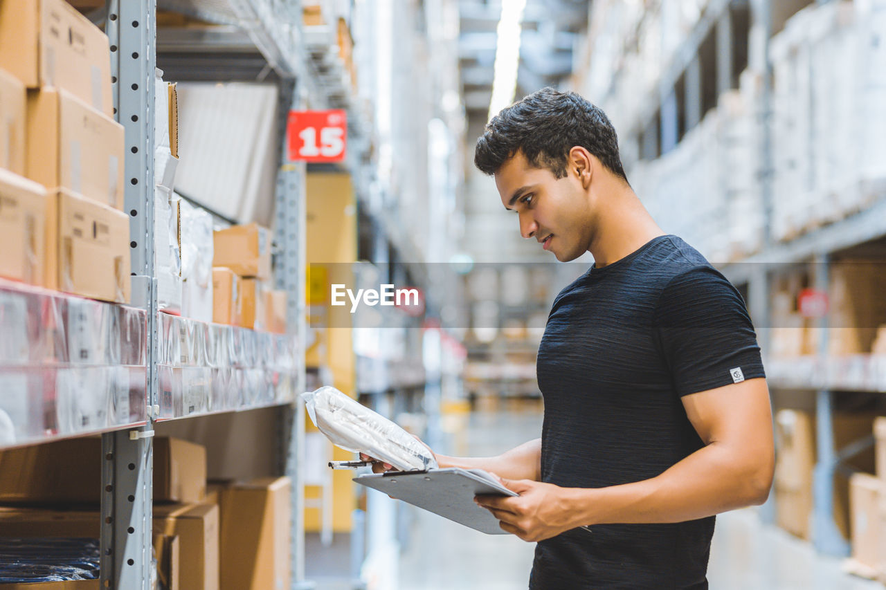 Young man looking at clipboard while standing in warehouse