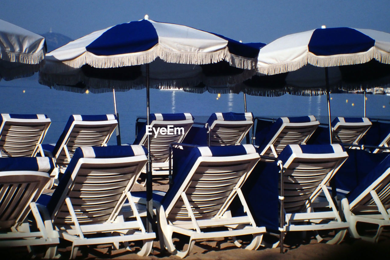 Deck chairs and beach umbrella in row against sky