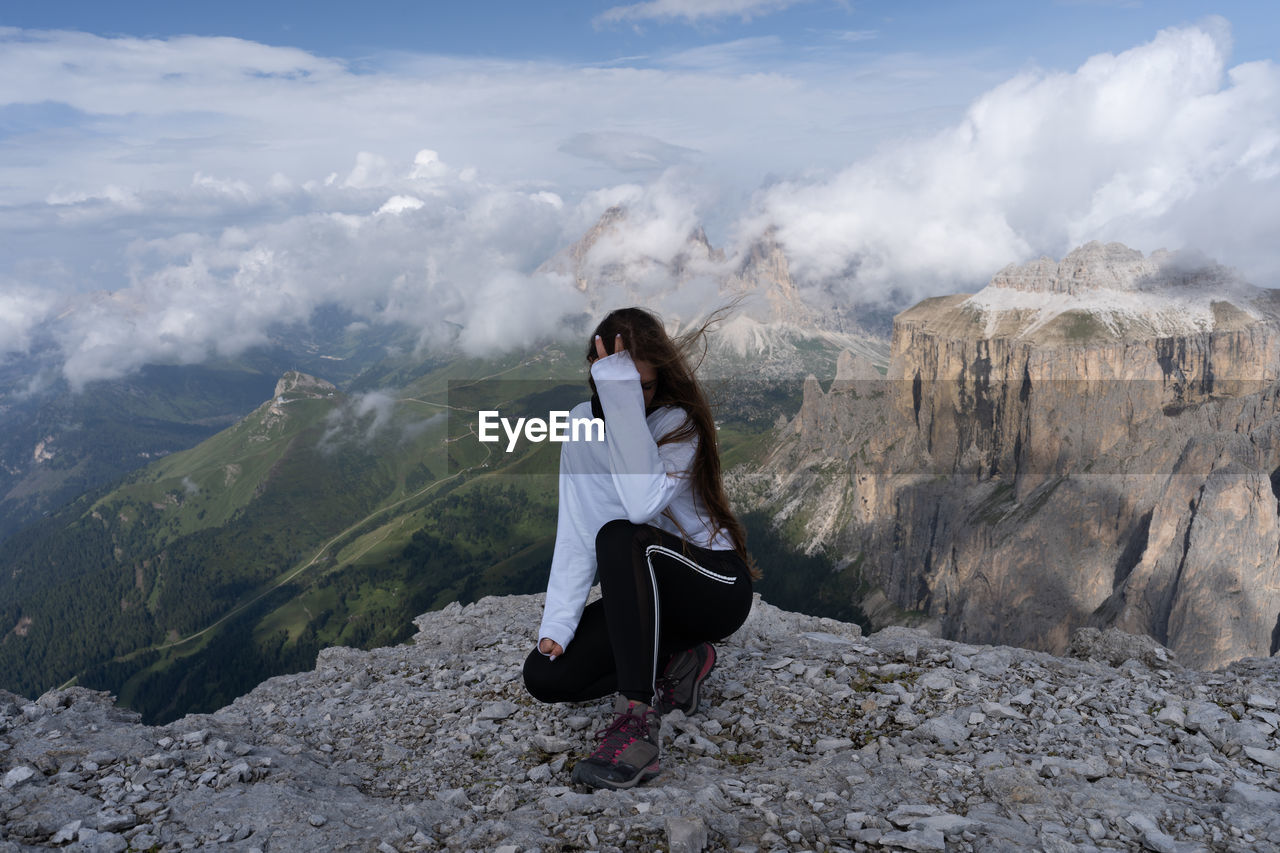 Full length of woman crouching at cliff against mountains