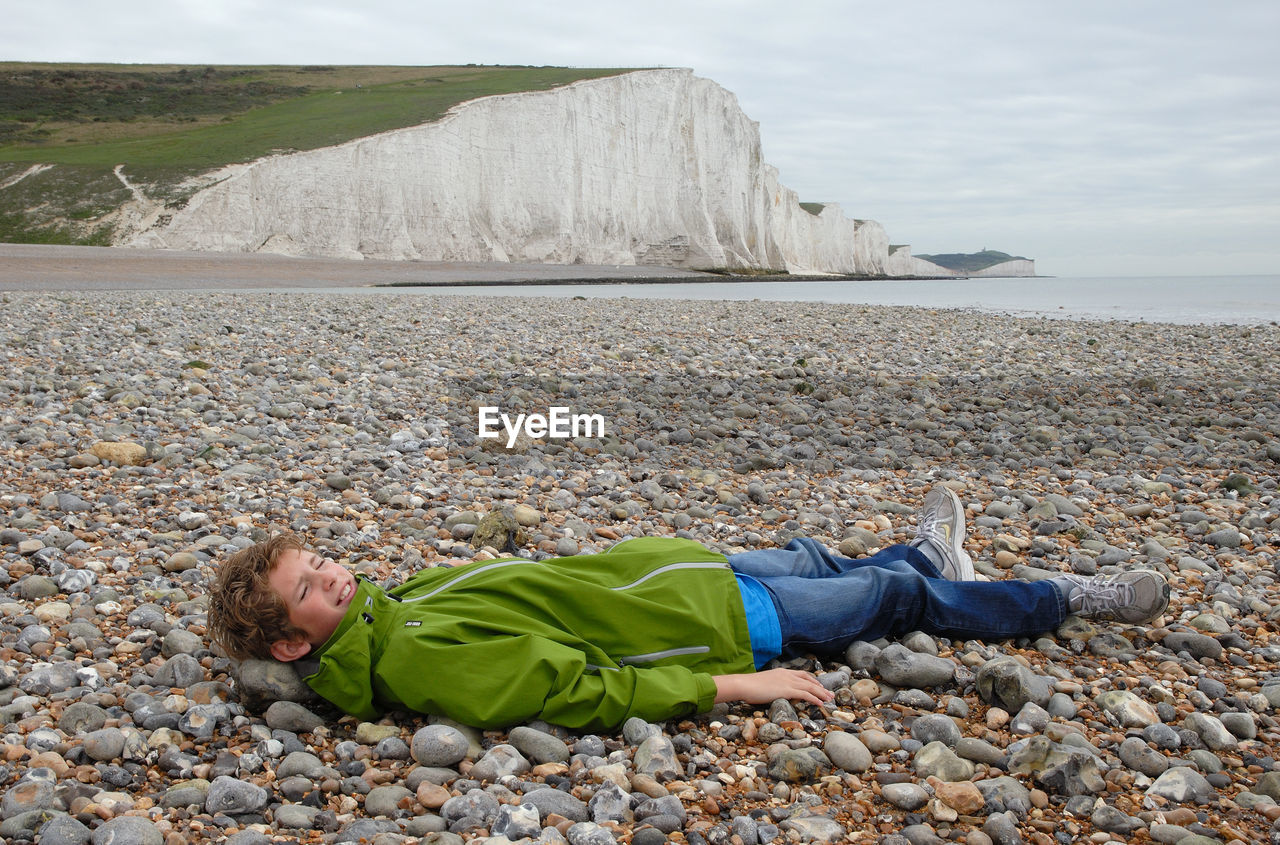 Full length of young man lying on pebbles at beach