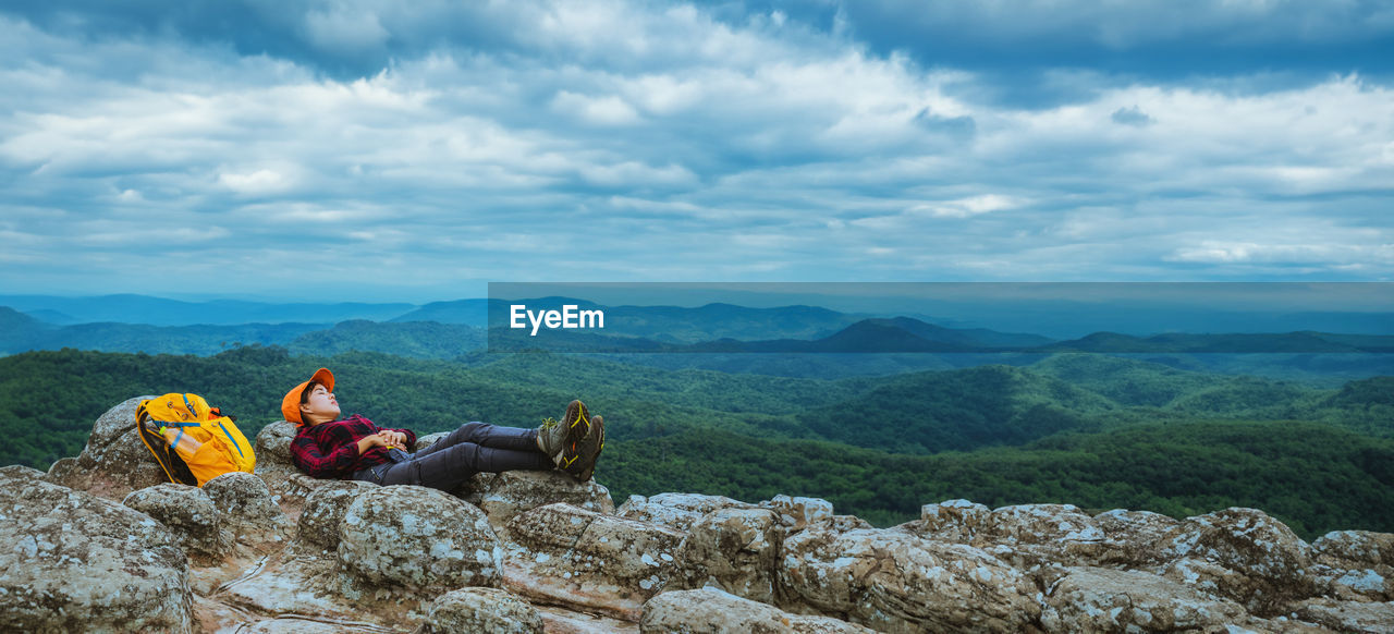 rear view of woman sitting on rock formations against sky