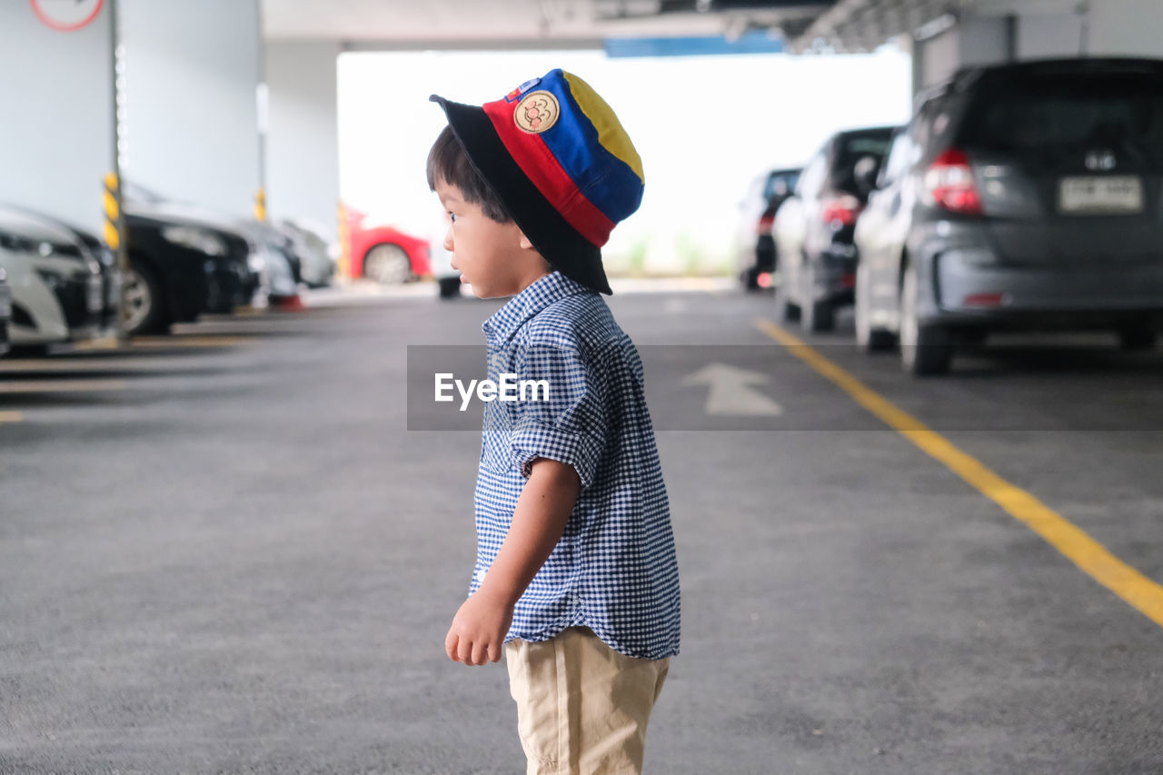 BOY STANDING ON ROAD IN CITY