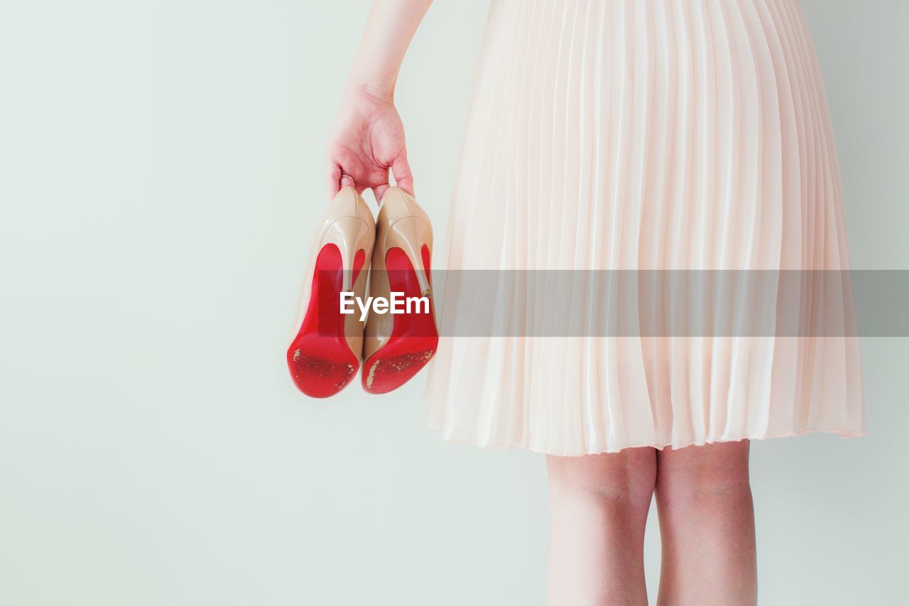 Rear view of woman holding high heels against wall