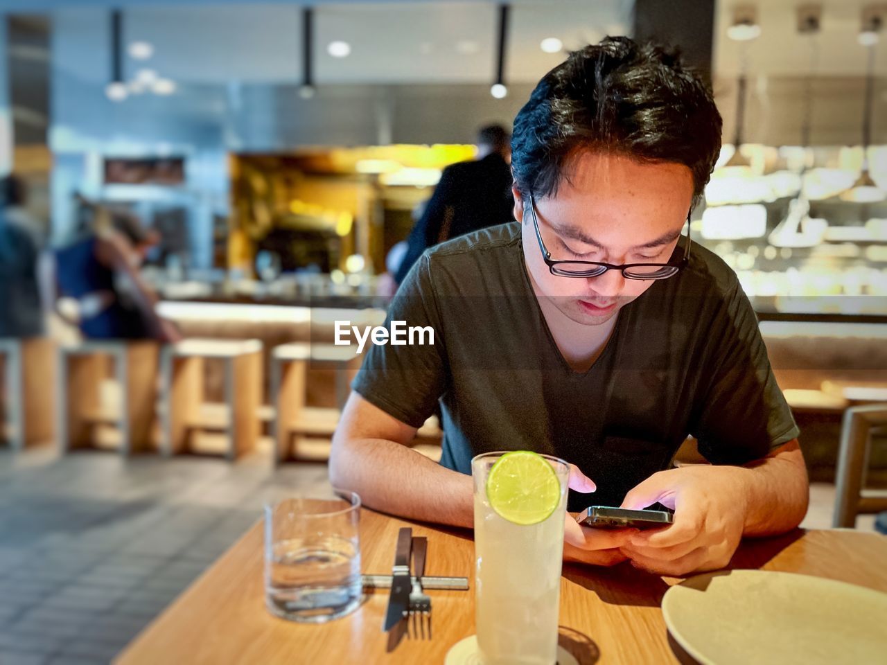 Young asian man using mobile phone at table inside restaurant.