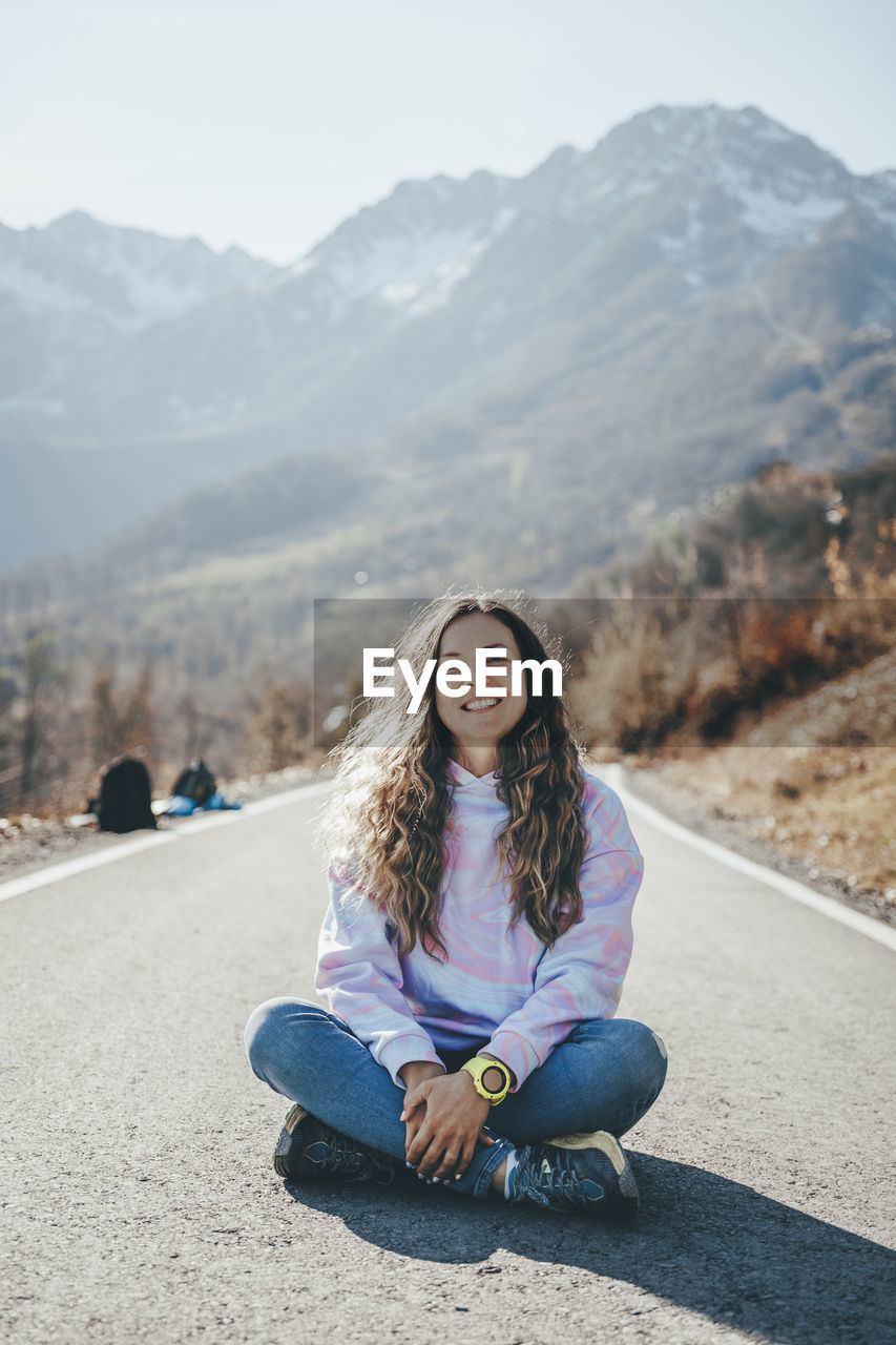 Carefree woman sitting cross-legged on road in front of mountains