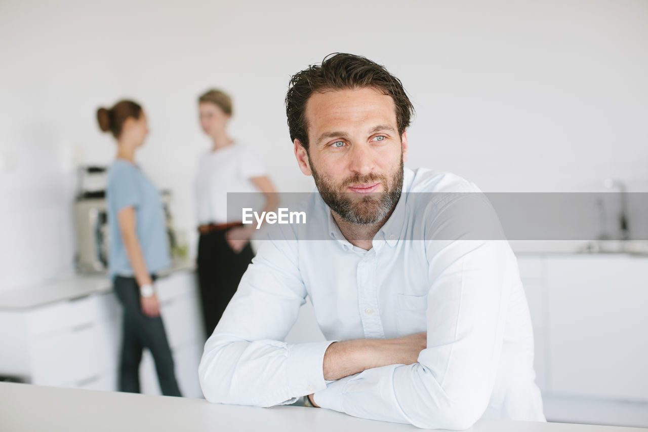 Mid adult man in office, people on background