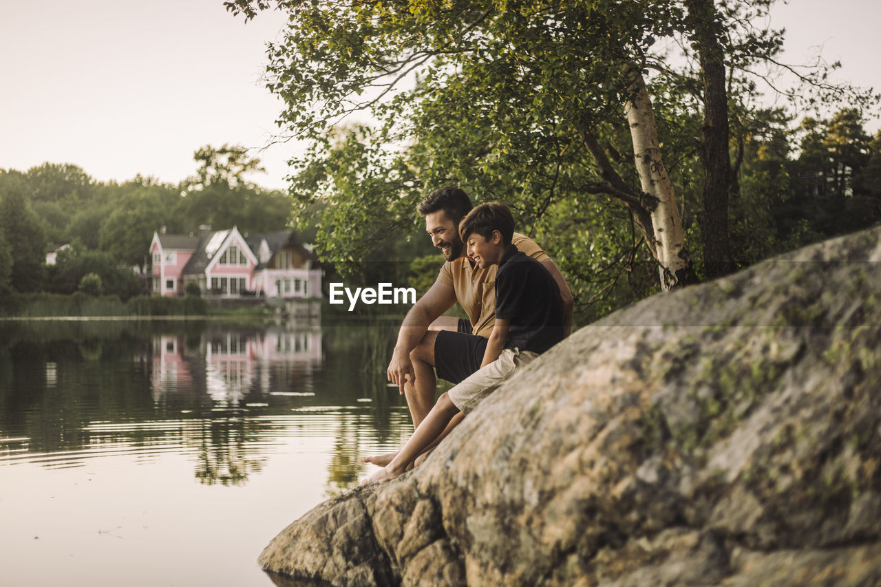 Father and son sitting on rock near lake