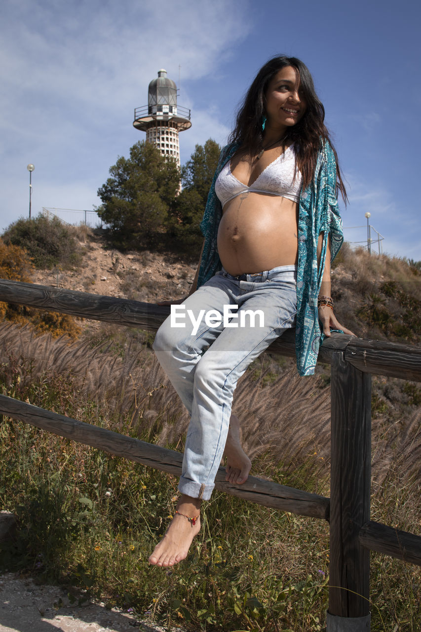 Portrait of beautiful pregnant woman against sky with a lighthouse behind 