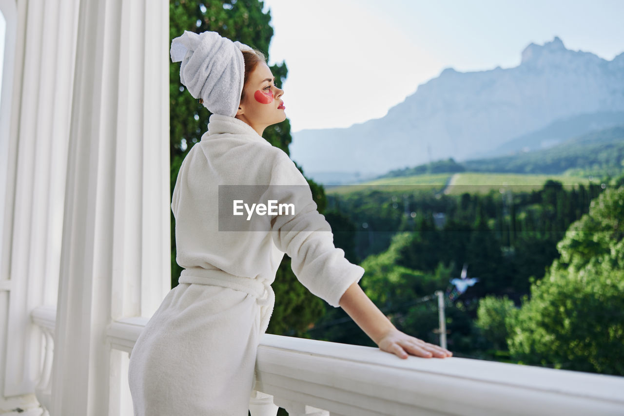 one person, adult, nature, standing, young adult, mountain, day, lifestyles, clothing, women, outdoors, architecture, side view, sky, relaxation, leisure activity, white, person, three quarter length, railing, plant, looking, environment, waist up, spring, female, beauty in nature