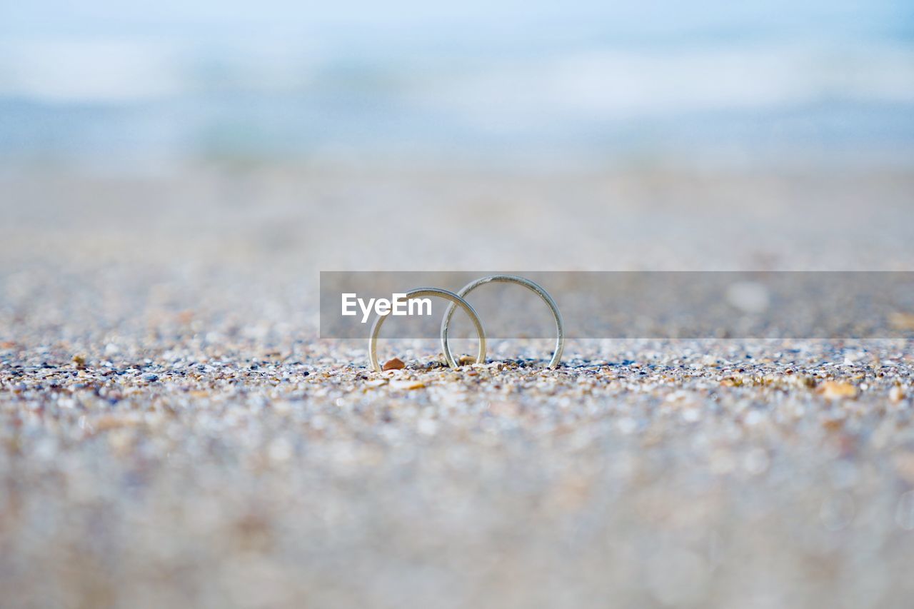 Surface level shot of wedding rings in sand at beach during sunny day
