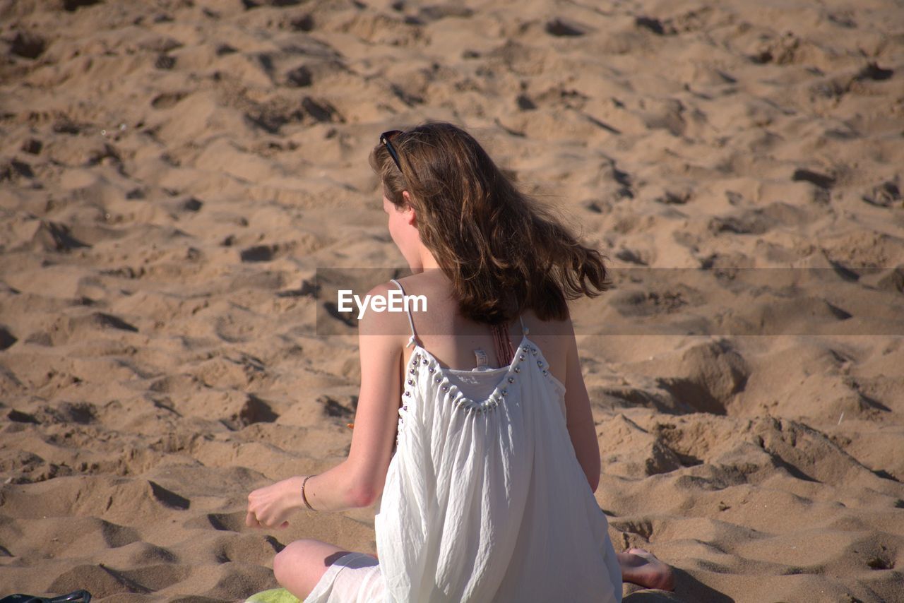 Rear view of woman sitting on sand at beach