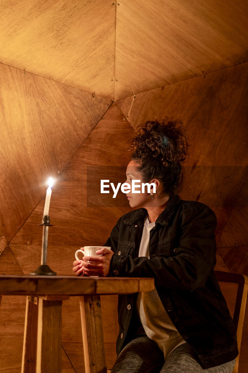 Woman having a cup of coffee sitting inside a dome tent.