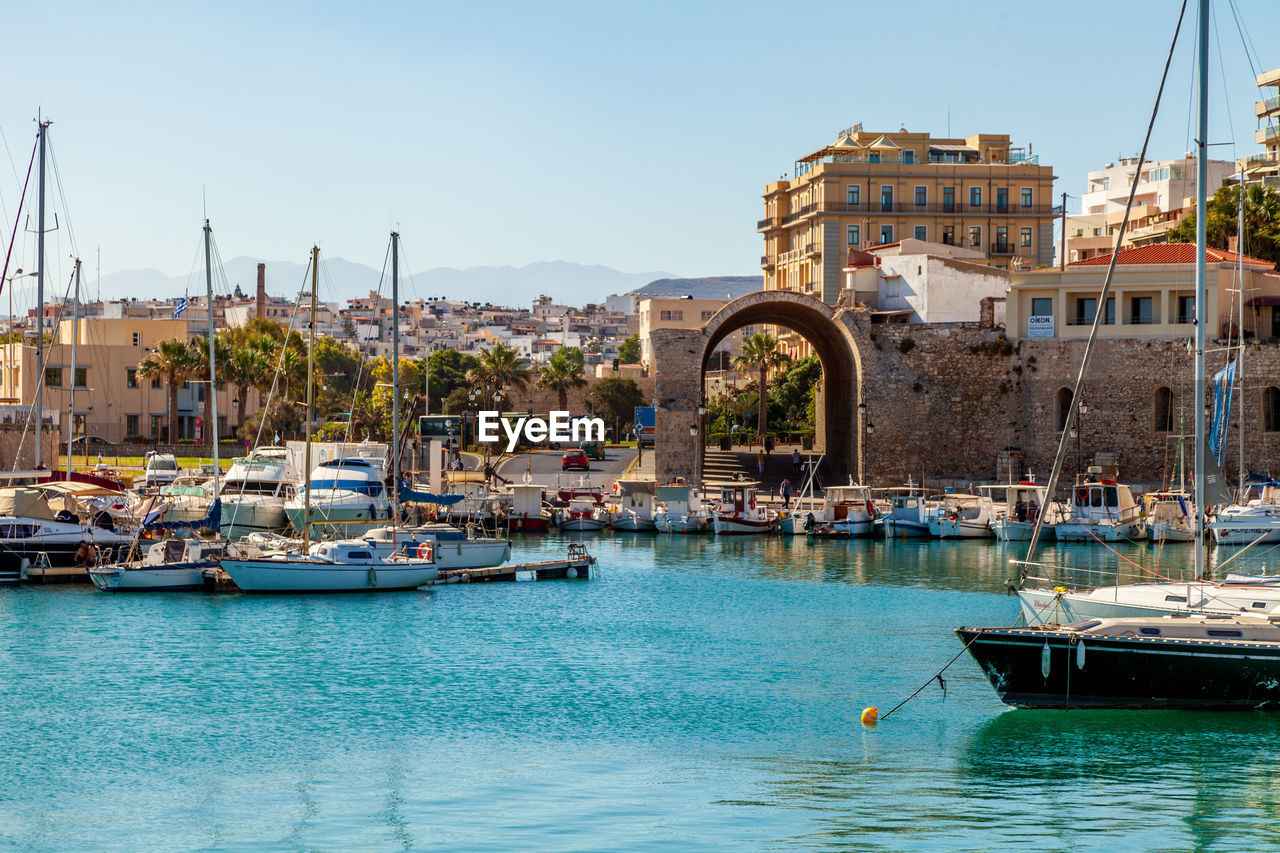 Sailboats moored in harbor by buildings against clear sky