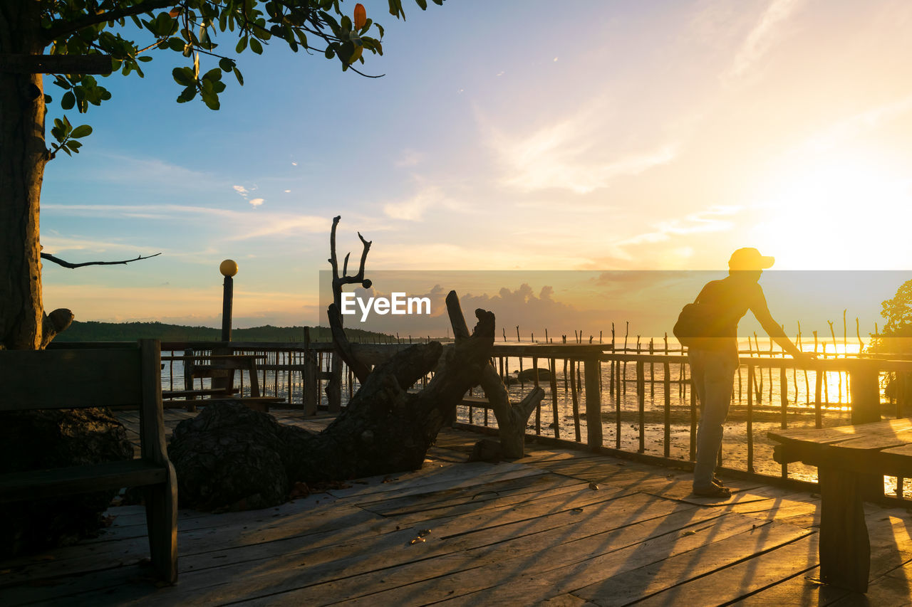 Full length of man looking at sea while standing on pier against sky during sunset