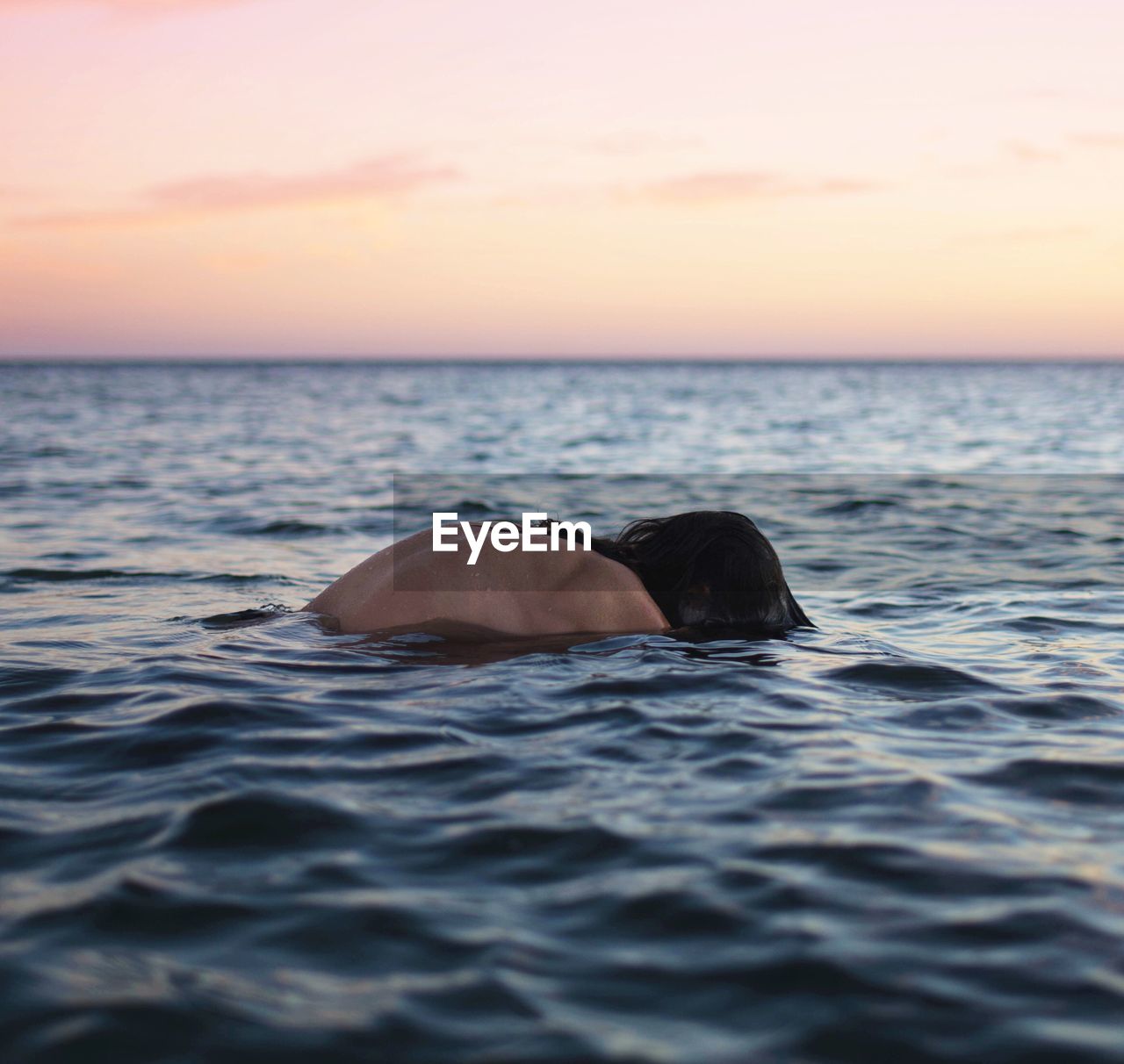 Shirtless person swimming in sea against sky during sunset