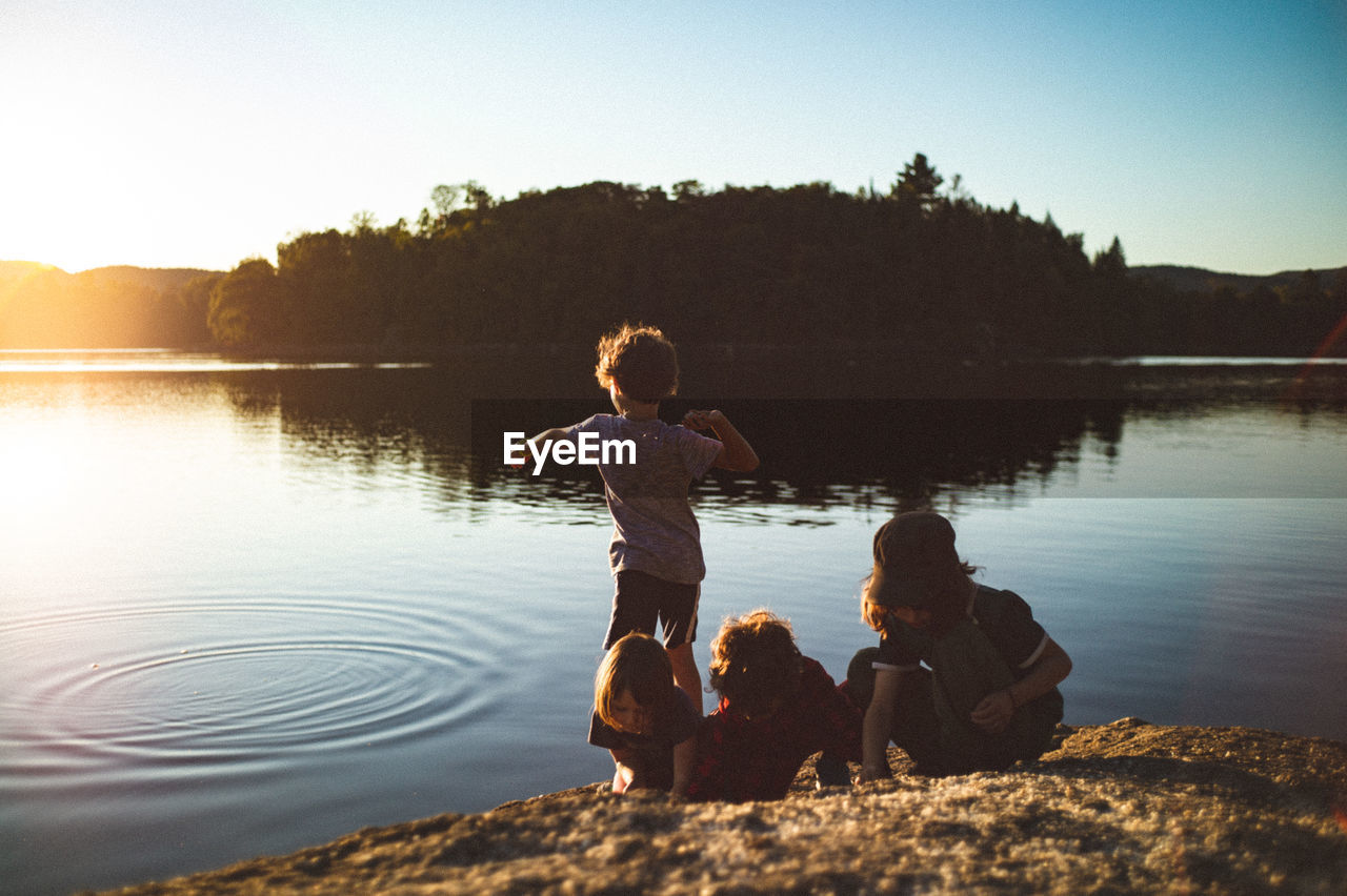 Rear view of children playing by lake against sky