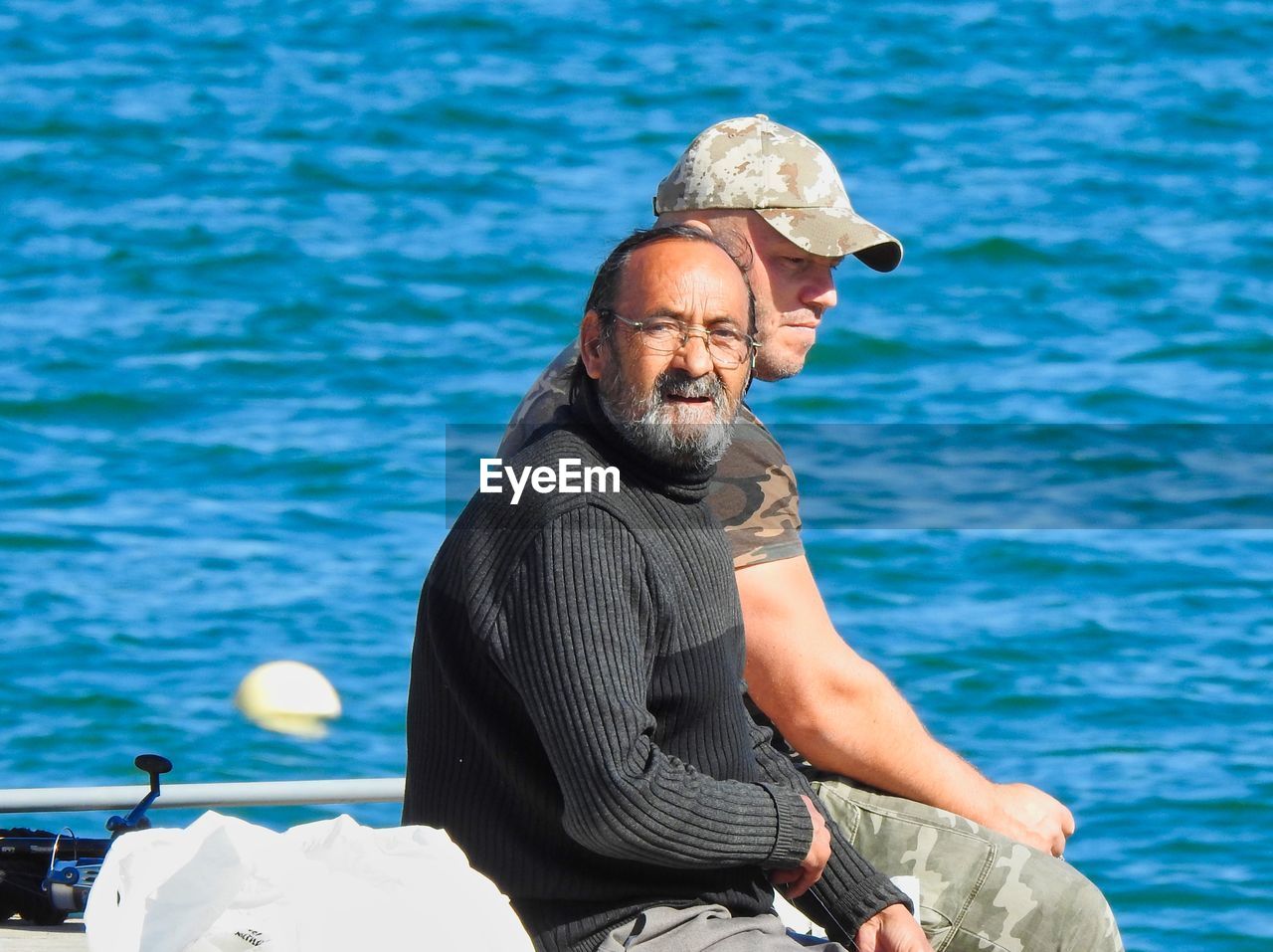 PORTRAIT OF MAN SITTING BY SEA AGAINST SKY