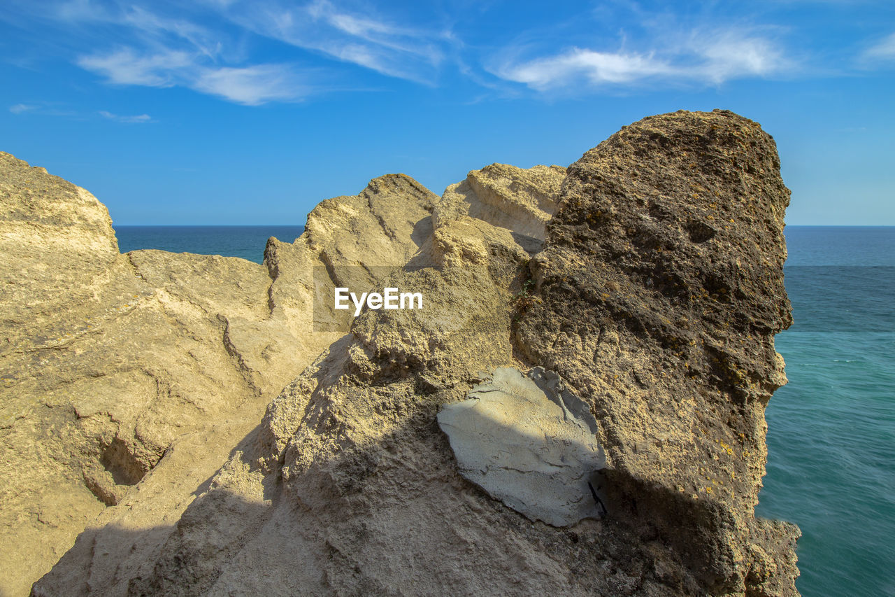 Rocks on shore by sea against blue sky