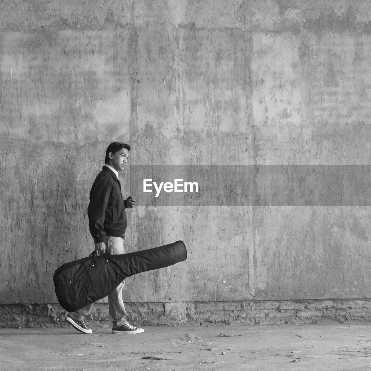 Full side view of a man carrying a guitar on the wall