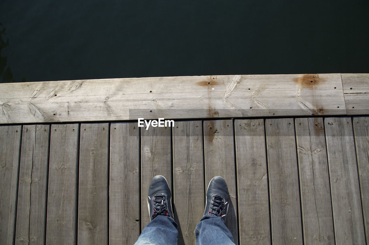 Low section of man standing on pier by lake