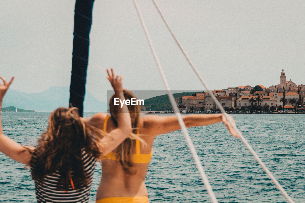 Women enjoying while standing on boat in sea against sky