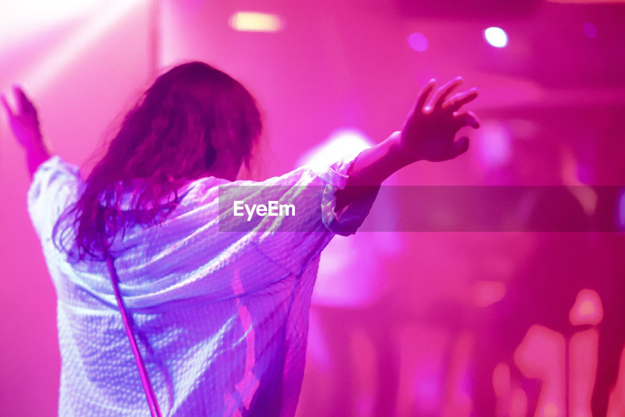 REAR VIEW OF WOMAN DANCING AGAINST ILLUMINATED WALL