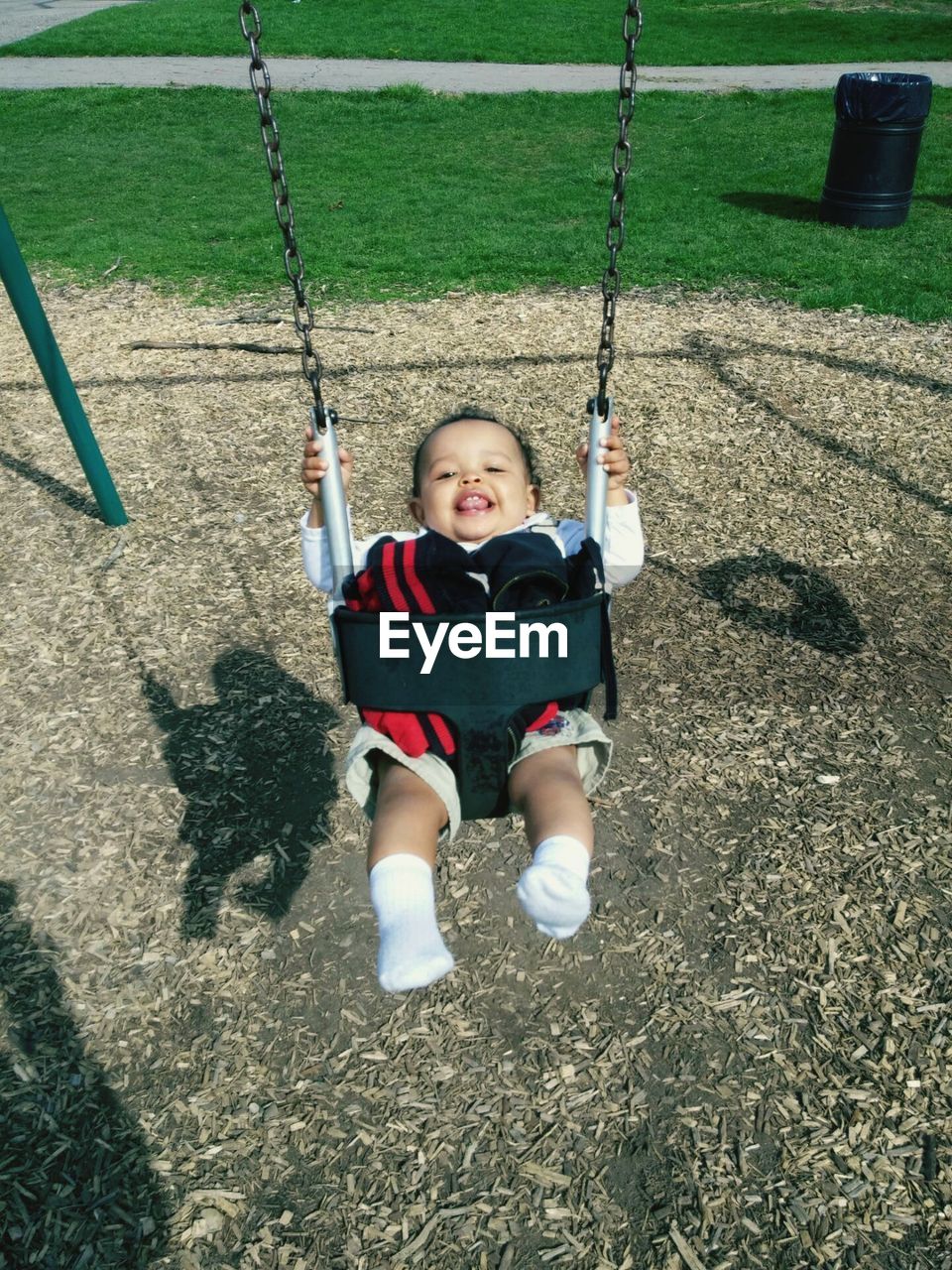 Portrait of cheerful toddler on swing in playground