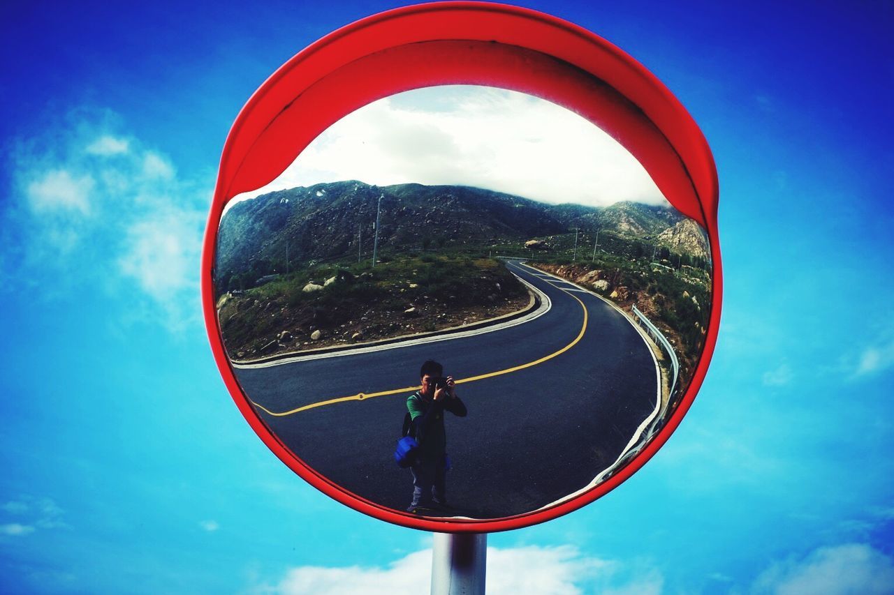 Reflection of man and road on traffic mirror against sky